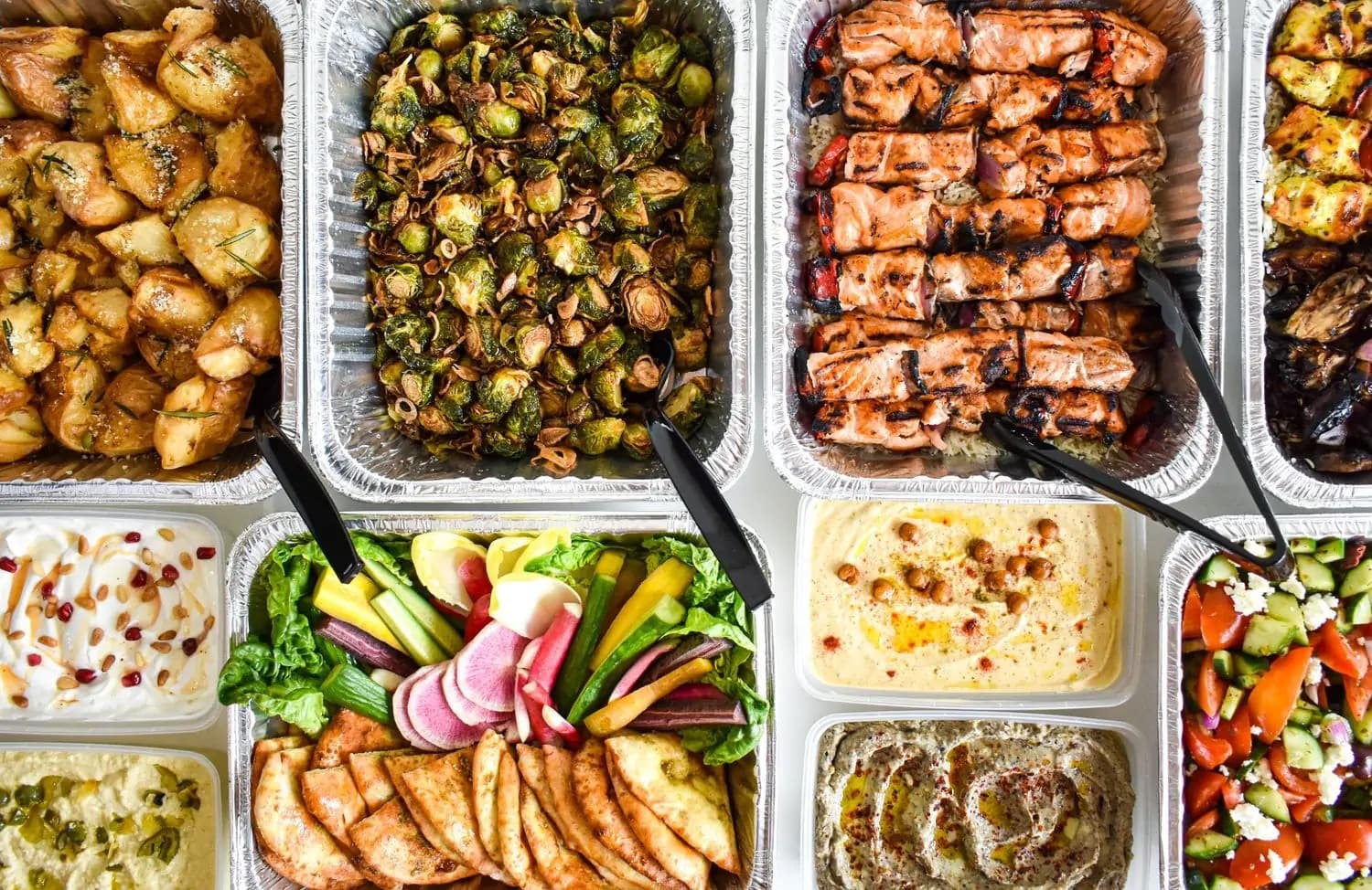 A Mediterranean catering spread of grilled skewers, hummus, tabbouleh, and roasted vegetables